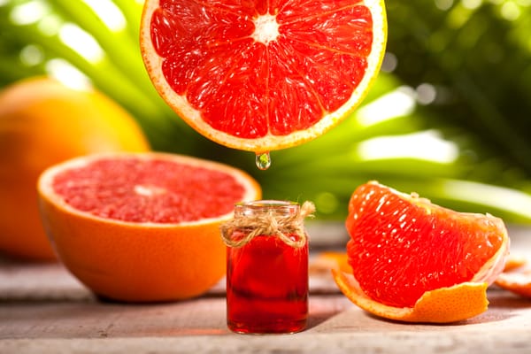 Bottle of essential oil from grapefruits on wooden table and green leaves background - alternative medicine